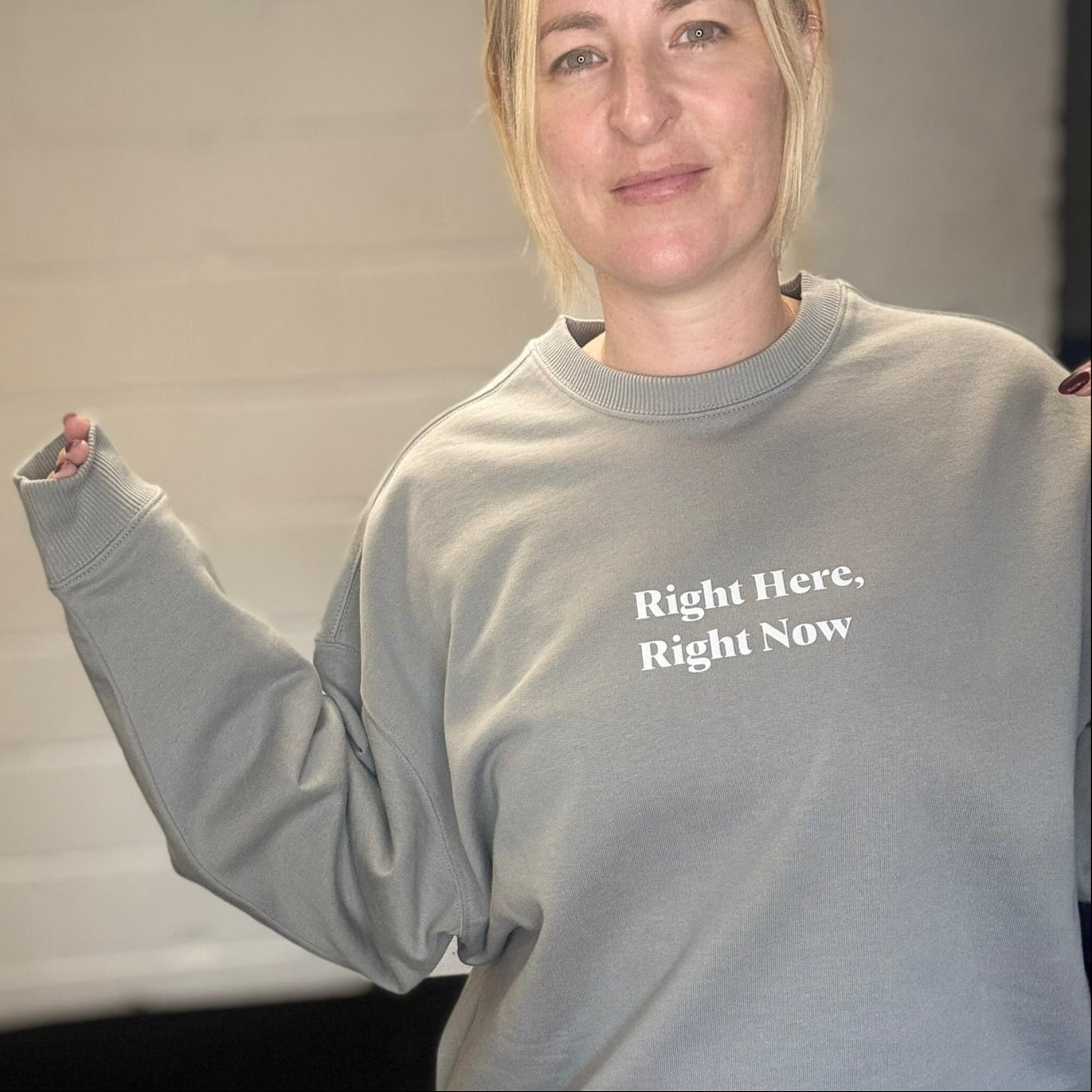 Person wearing a gray sweatshirt with text, standing against a neutral background