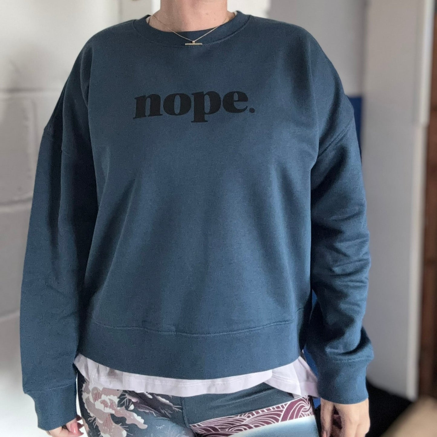 Person wearing a blue sweatshirt with 'nope.' text in a casual setting