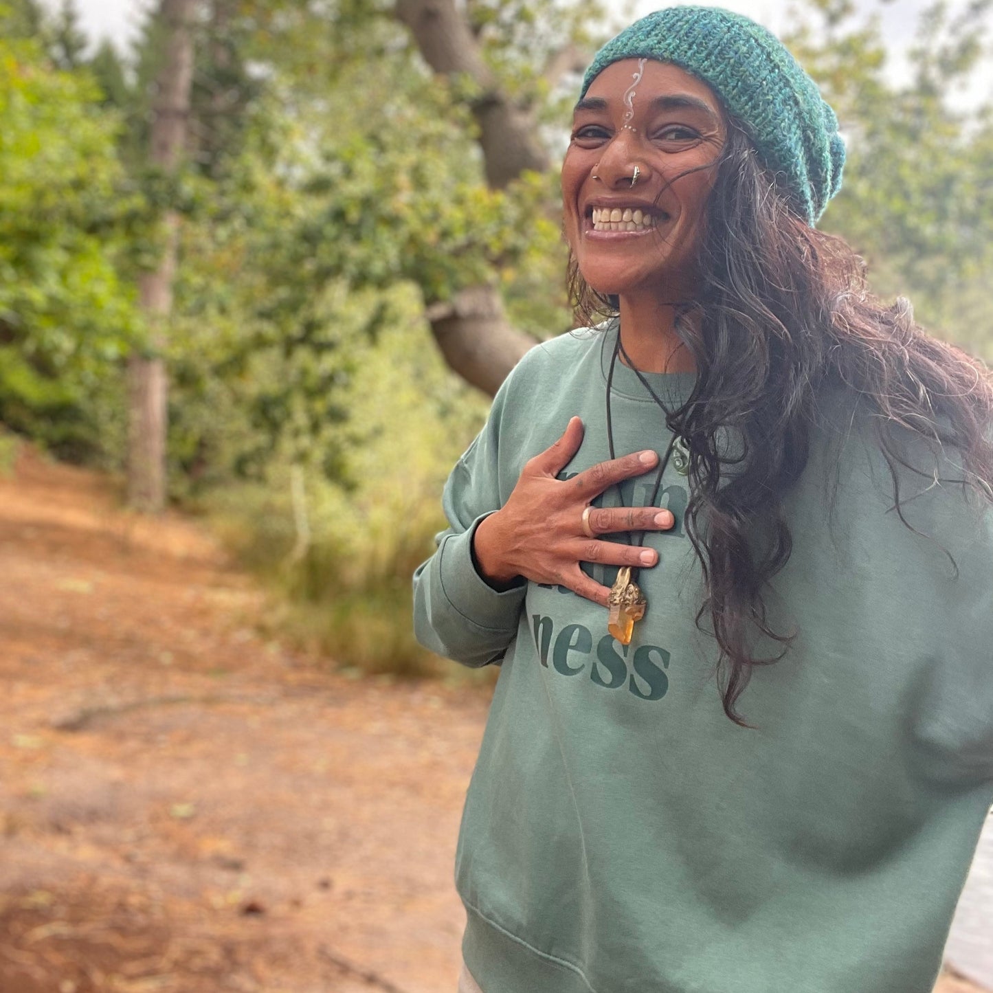 Person wearing a green sweatshirt and beanie outdoors with trees in the background