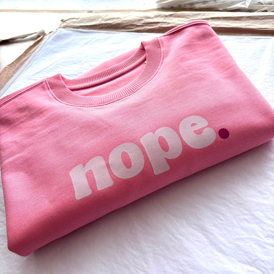 Folded pink this is mabel sweatshirt with 'nope.' text on a white surface