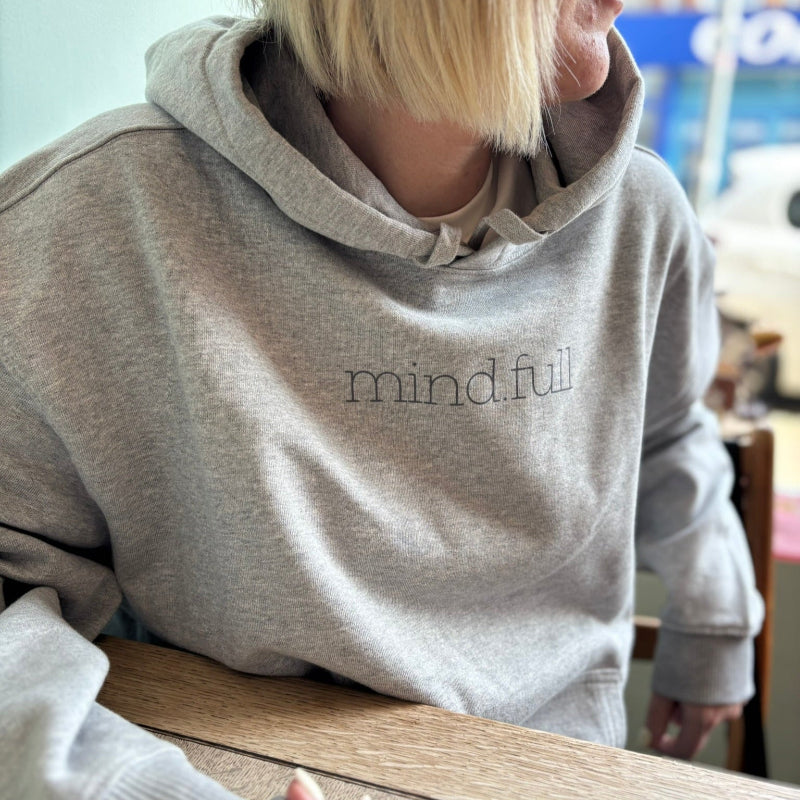 Model wearing mind.full hoodie sitting in soft light – mindfulness-inspired clothing