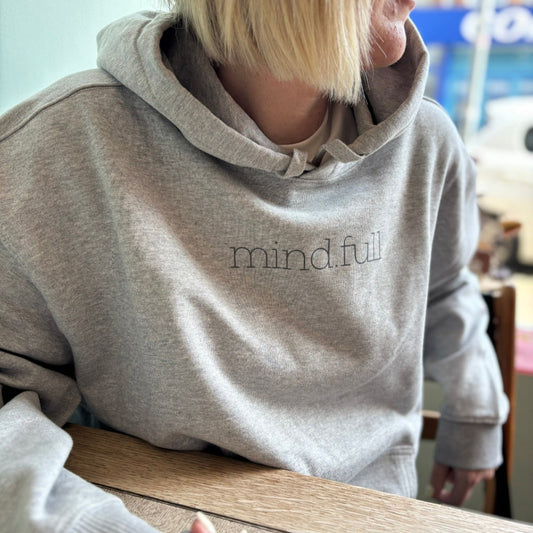 Model wearing mind.full hoodie sitting in soft light – mindfulness-inspired clothing