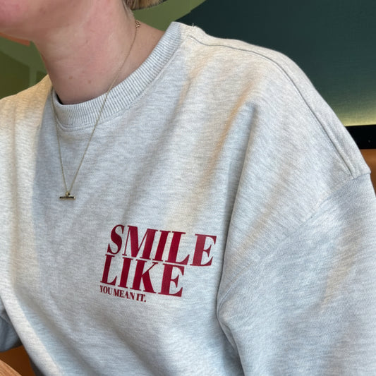 Person wearing a This is Mabel grey sweatshirt with 'SMILE LIKE YOU MEAN IT' text, sitting at a table.