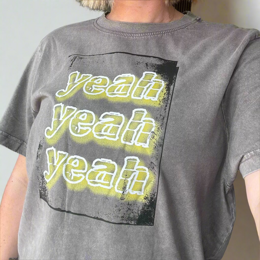 Person wearing a gray t-shirt with 'yeah yeah yeah' text in yellow.