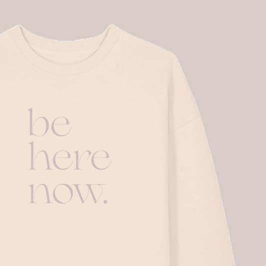 Beige sweatshirt with 'be here now' text on a gray background, featuring the brand 'MABEL'.