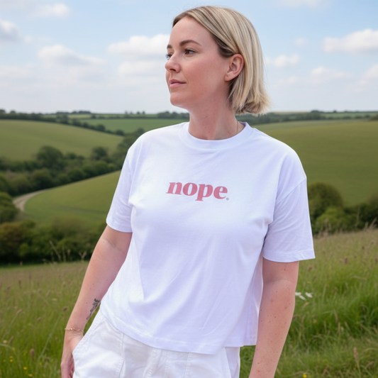 Person wearing a this is mabel boxy white t-shirt with 'nope' printed on it at the beach.
