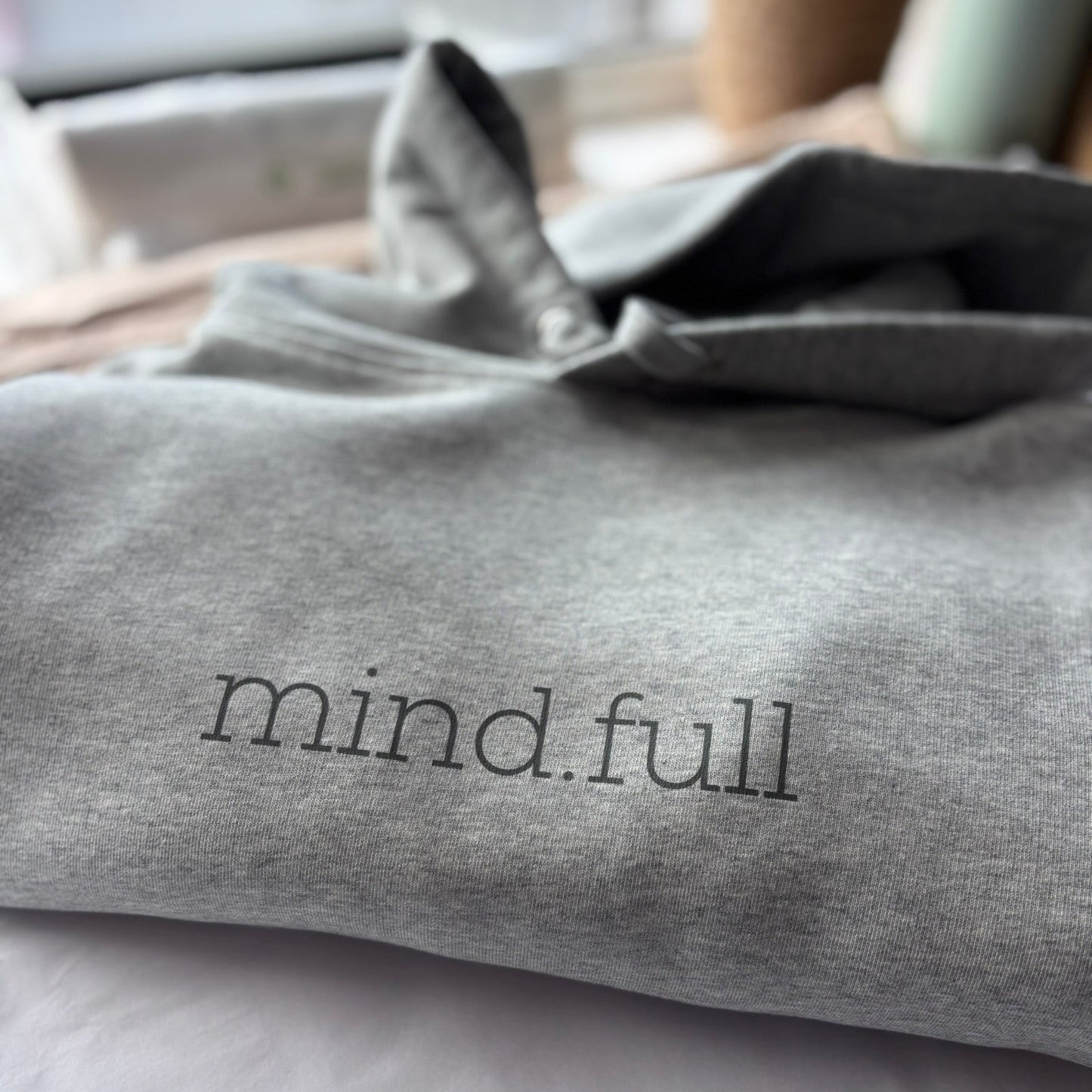 Gray sweatshirt with 'mind.full' text on a white surface