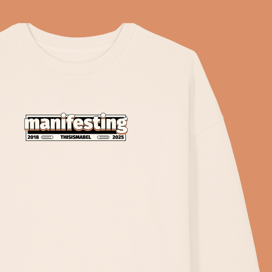 White sweatshirt with 'manifesting' text on a beige background