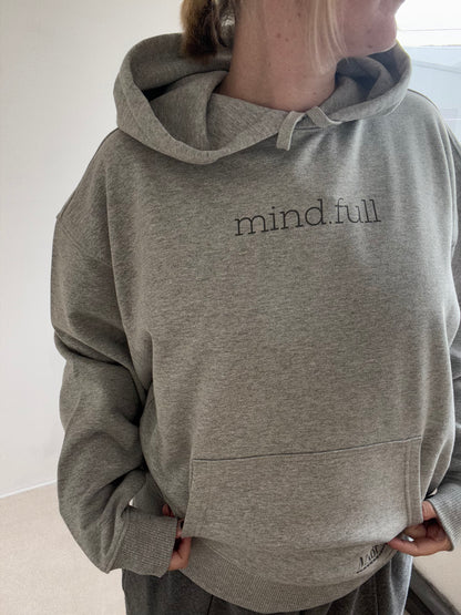 Person wearing a this is mabel heather grey hoodie with 'mindful' print on a white background