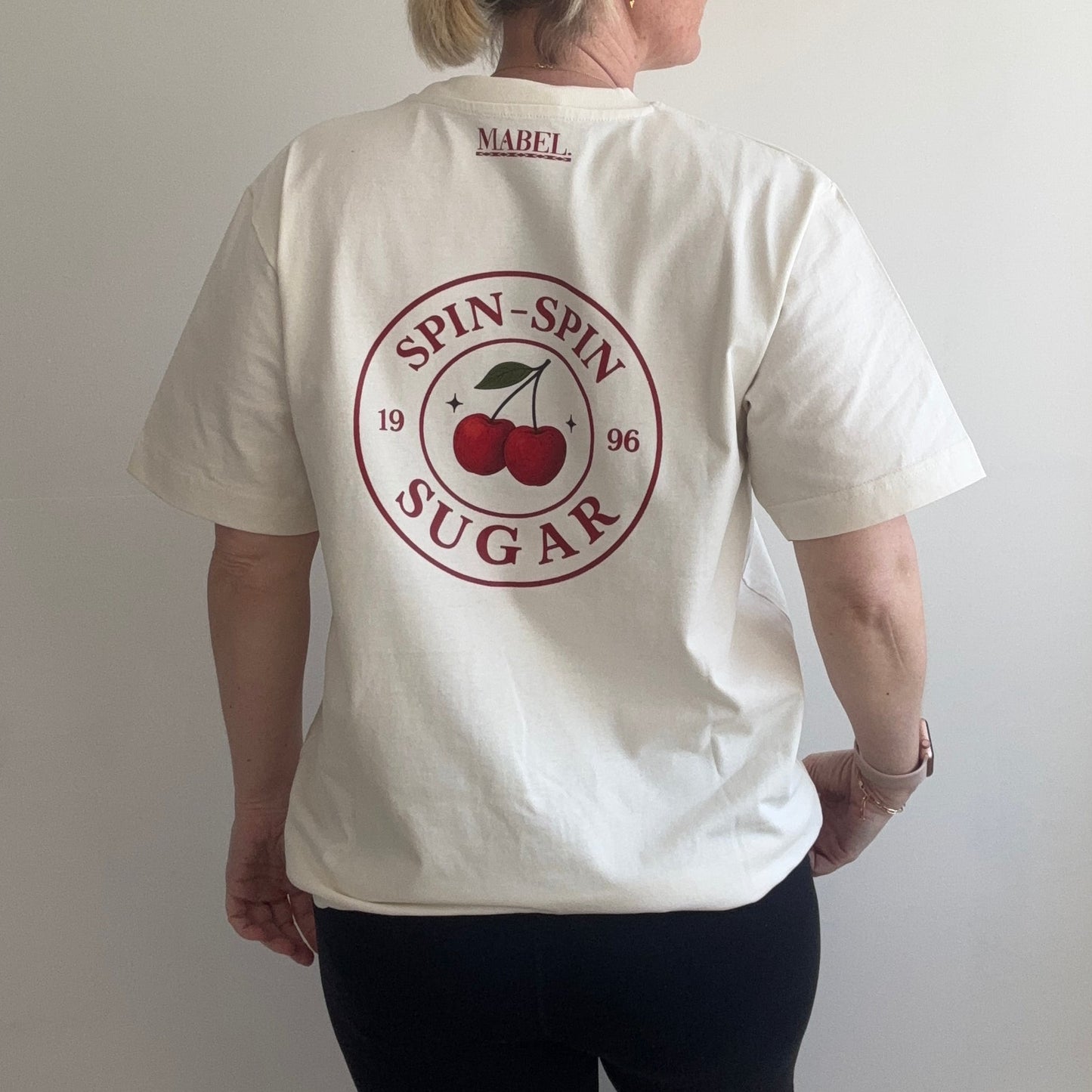 Person wearing a cream t-shirt with a red logo on a plain background