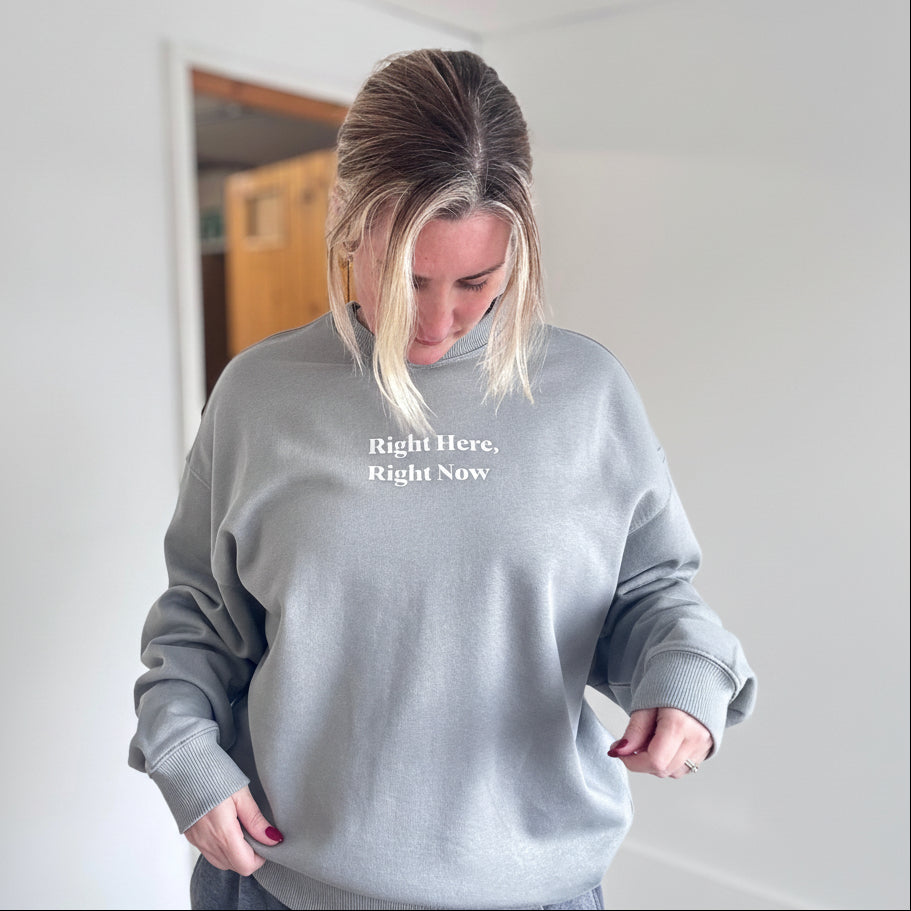 Person wearing a gray sweatshirt with text, standing indoors.
