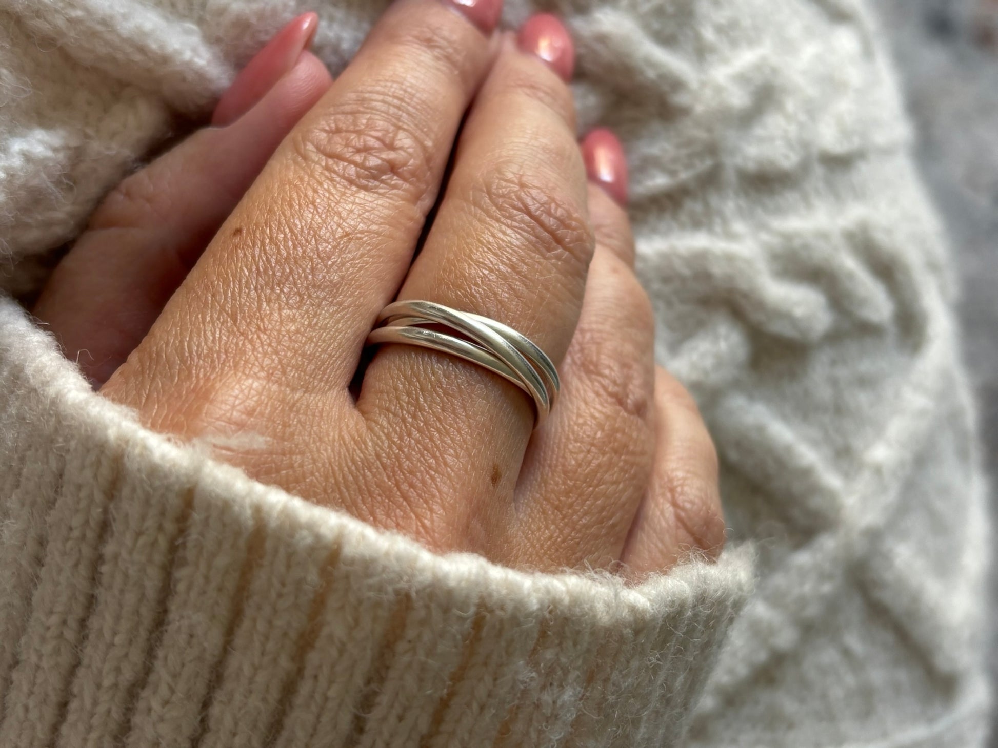 Hand wearing a silver ring with a textured beige background