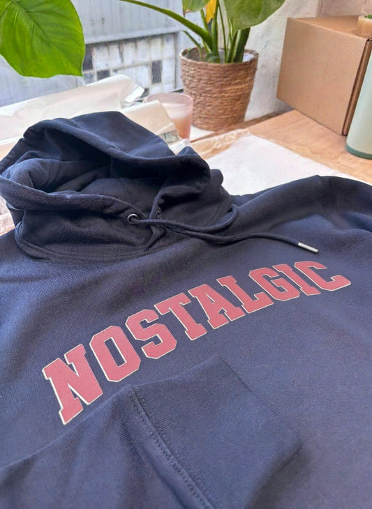 Navy hoodie with 'NOSTAGGIC' text on a surface with plants and boxes in the background