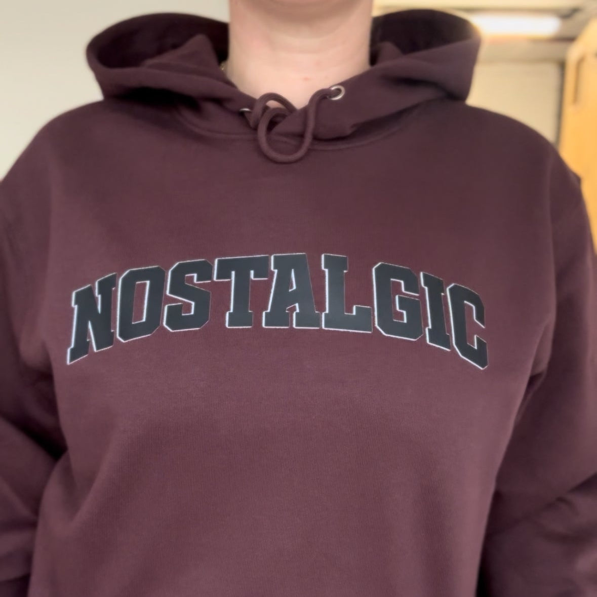 Person wearing a maroon hoodie with 'NOSTALGIC' text on a neutral background