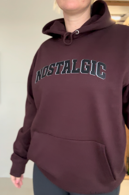 Person wearing a maroon hoodie with 'NOSTALGIC' text on a plain background