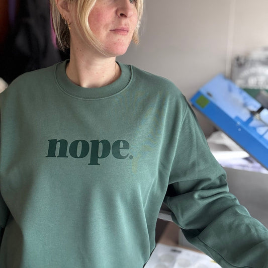 Person wearing a green sweatshirt with 'nope' text in an indoor setting