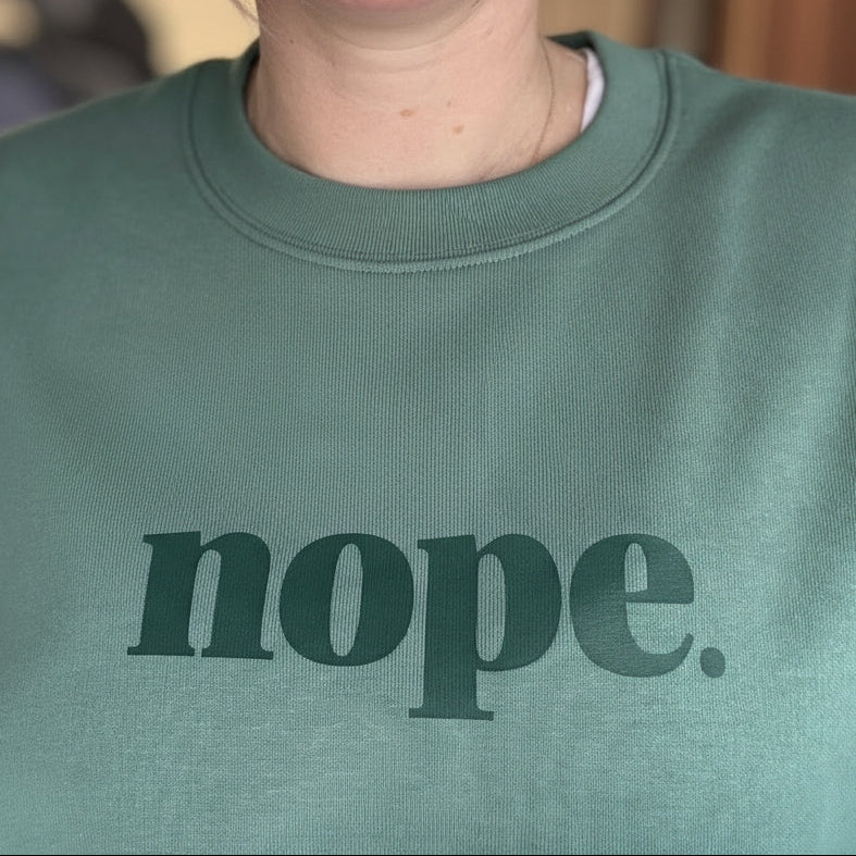 Person wearing a green sweatshirt with 'nope.' printed on it.