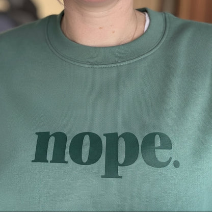 Person wearing a green sweatshirt with 'nope.' printed on it.