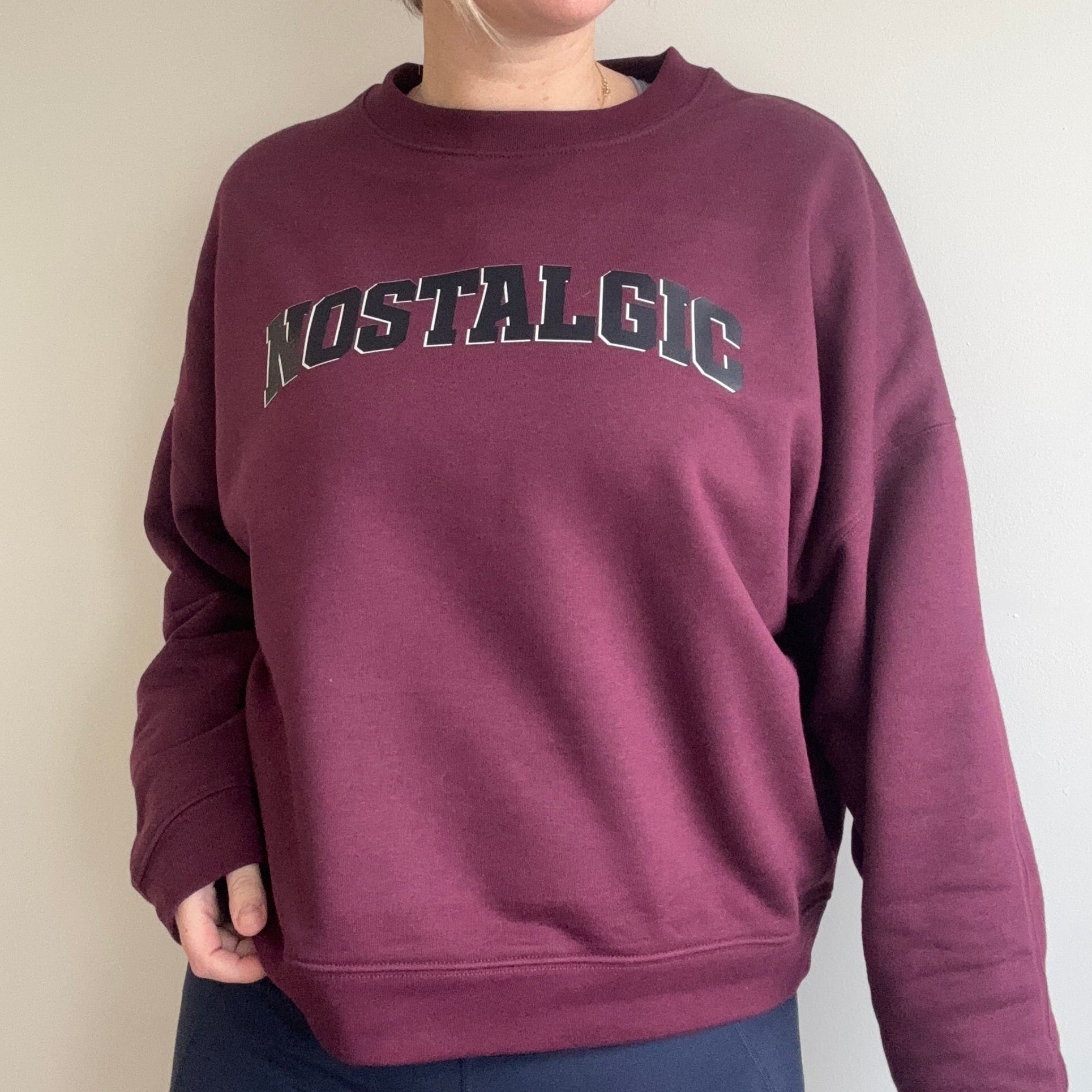 Person wearing a maroon sweatshirt with 'Nostalgic' text on a plain background