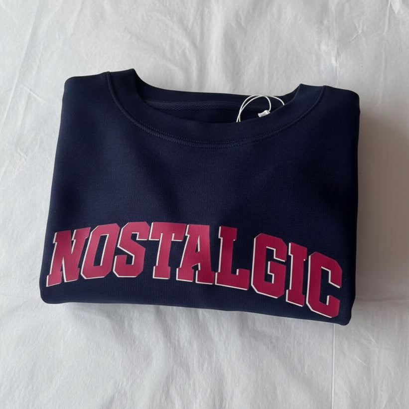 Folded navy blue sweatshirt with 'NOSTALGIC' text in red on a white surface.