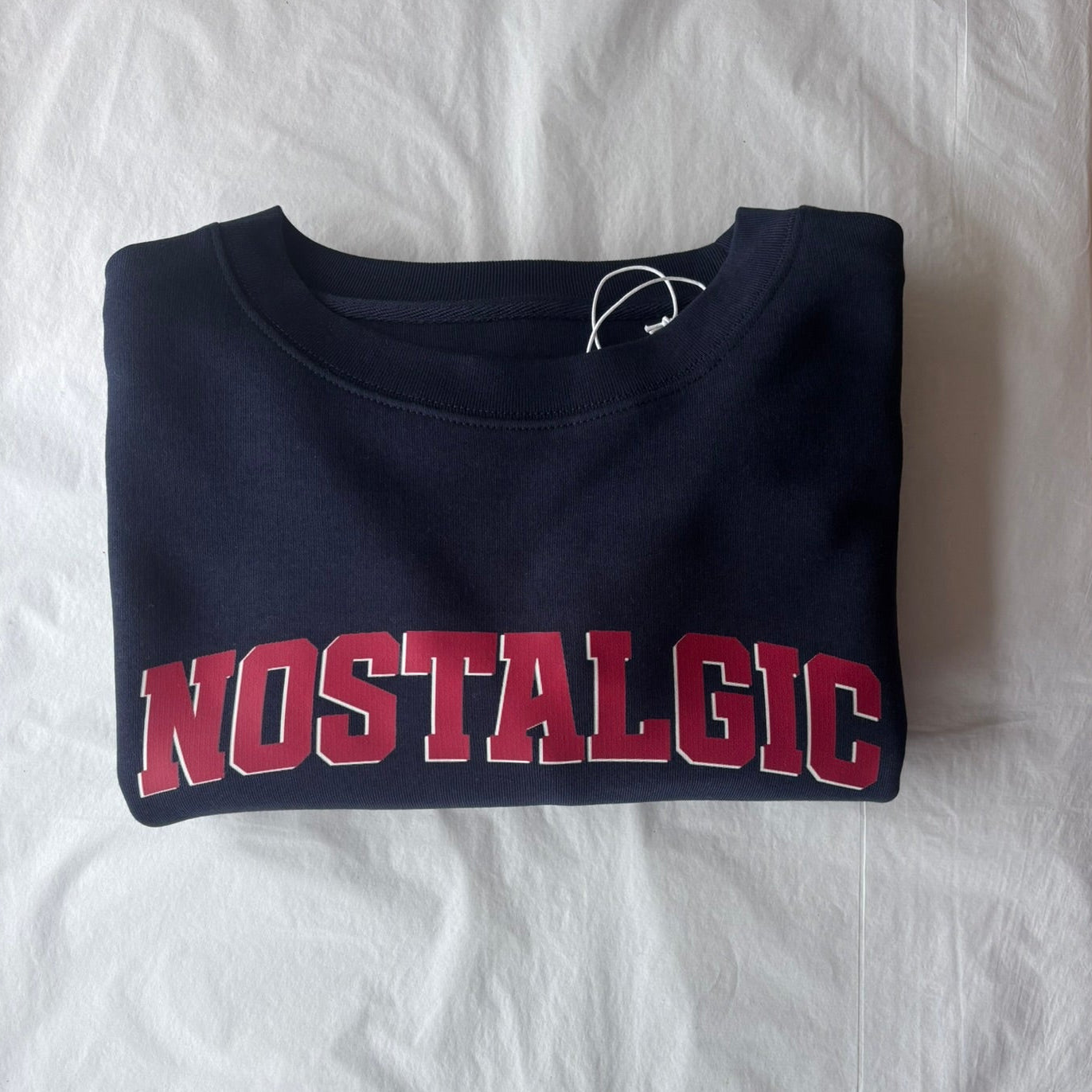 Folded navy blue sweatshirt with 'NOSTALGIC' text in red on a white background
