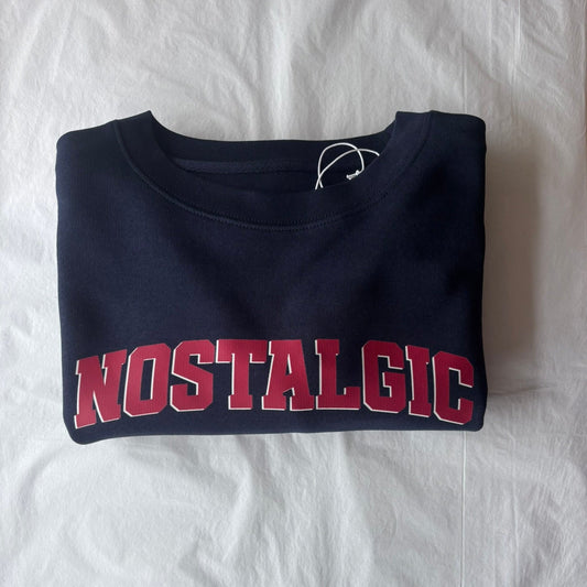 Folded navy blue sweatshirt with 'NOSTALGIC' text in red on a white background