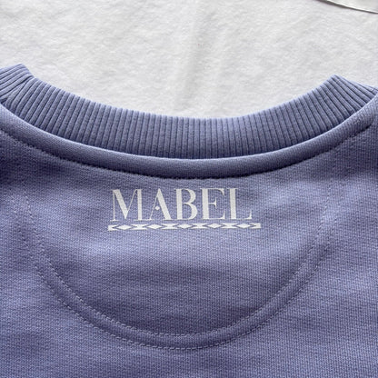 Close-up of a violet sweatshirt with 'MABEL' branding on a light grey background