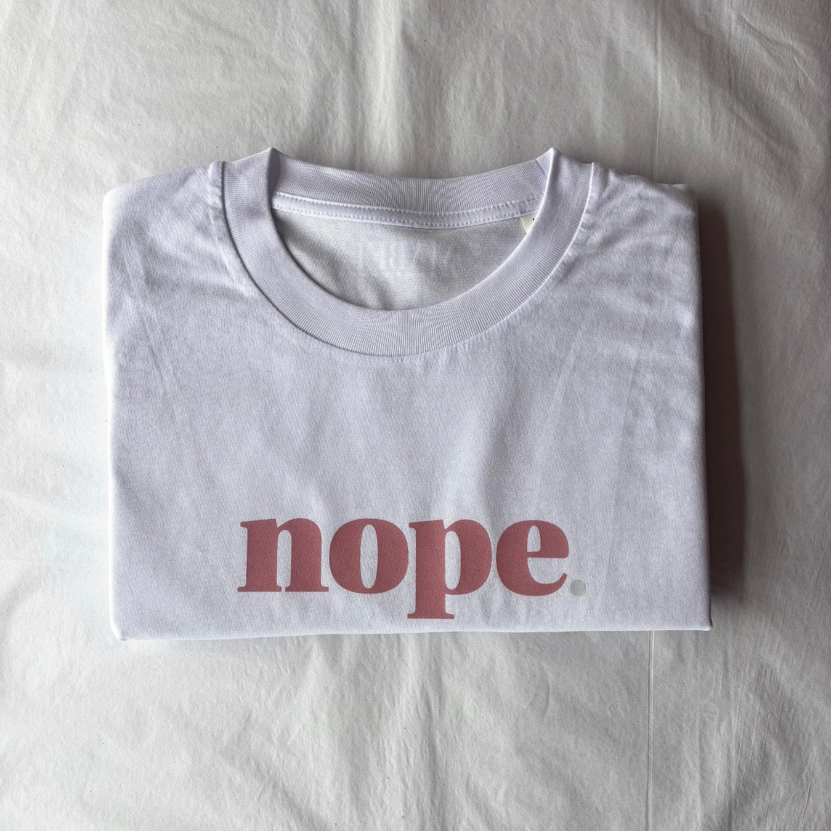 this is mabel White t-shirt with 'nope' printed on it, folded on a white surface