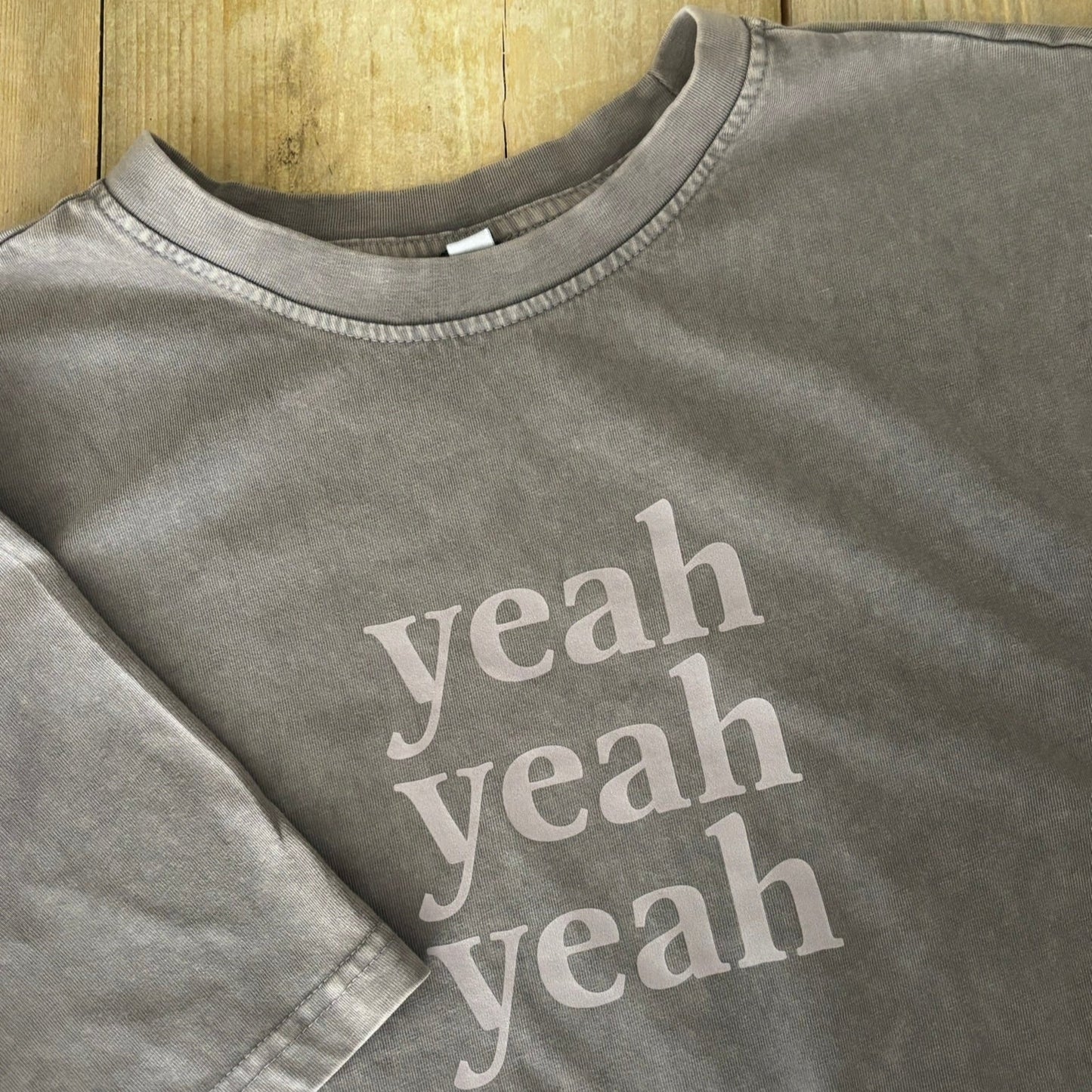 Gray sweatshirt with 'yeah yeah yeah' text on a wooden surface