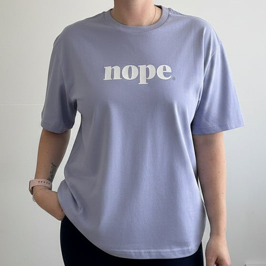 Person wearing a light purple t-shirt with 'nope.' text on a plain background