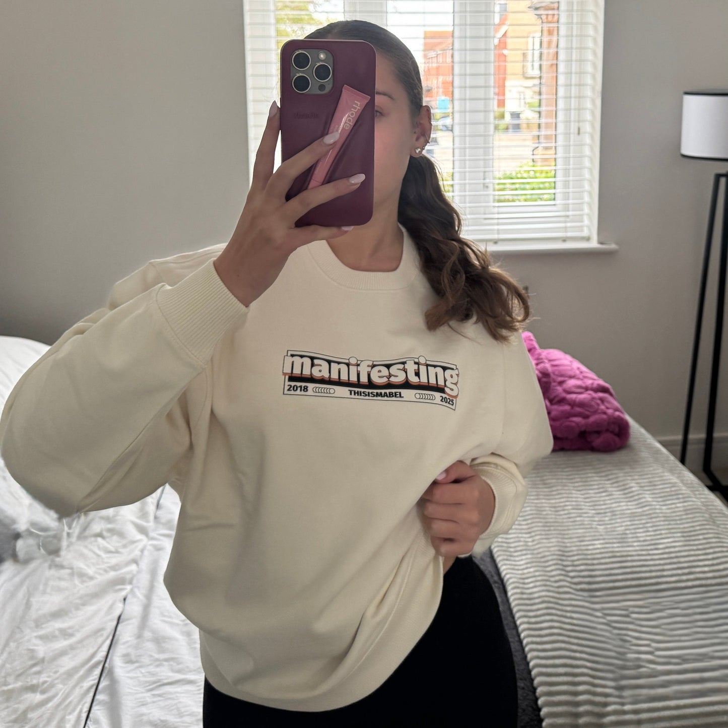 this is mabel cream sweatshirt retro manifesting print, taking a mirror selfie in a bedroom.