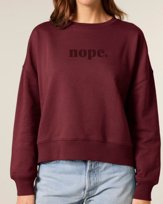 Maroon sweatshirt with 'nope.' text worn by a person on a beige background