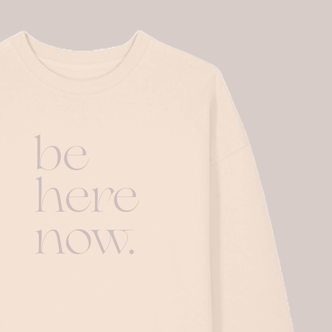 Beige sweatshirt with 'be here now' text on a gray background, featuring the brand 'MABEL'.