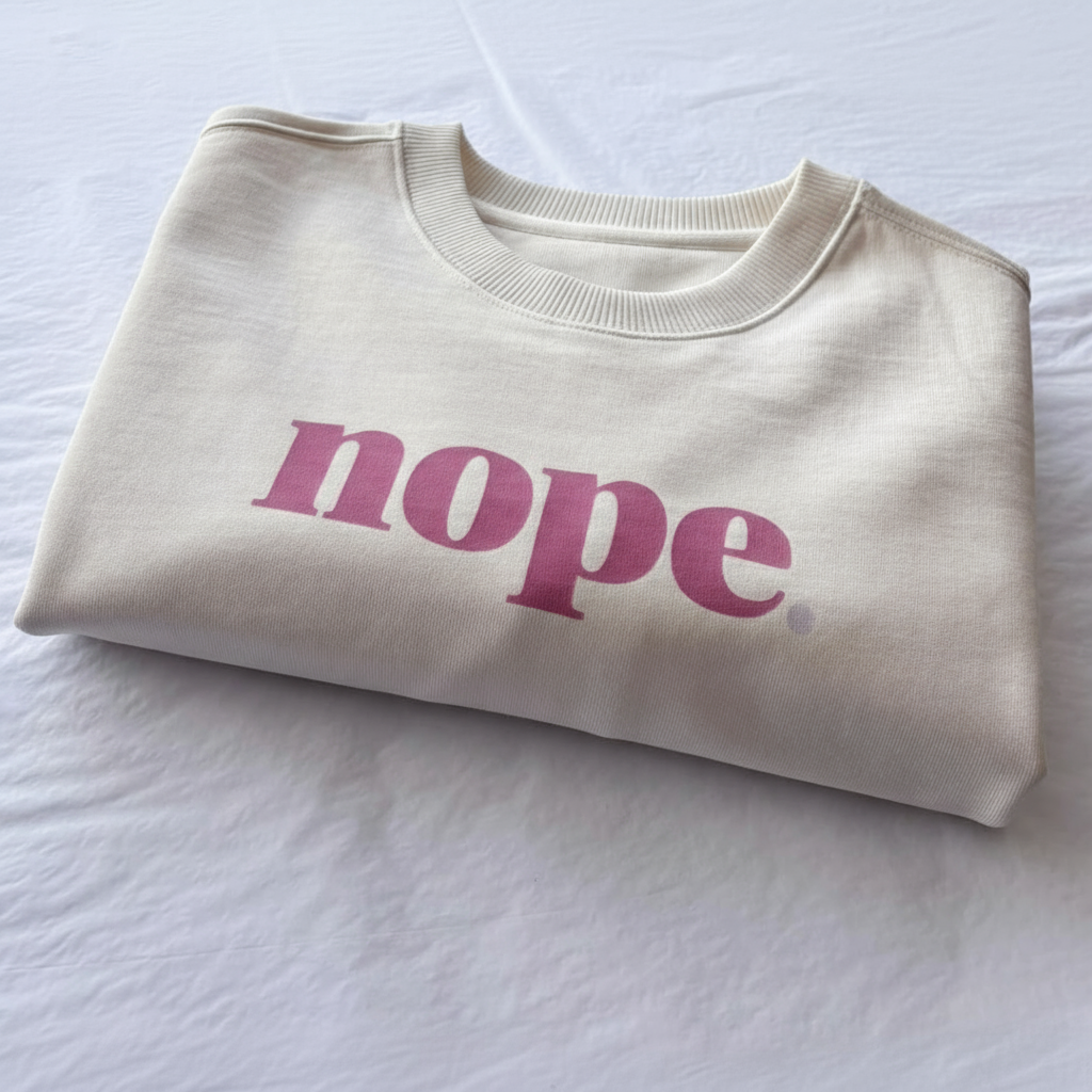 Folded cream this is mabel oversized  sweatshirt with 'nope' in pink text on a white surface