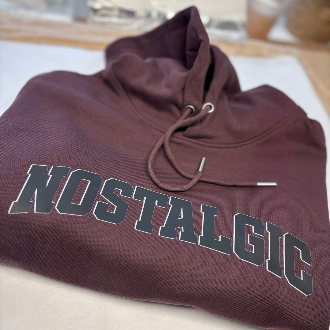 Maroon hoodie with 'NOSTALGIC' text on a white surface