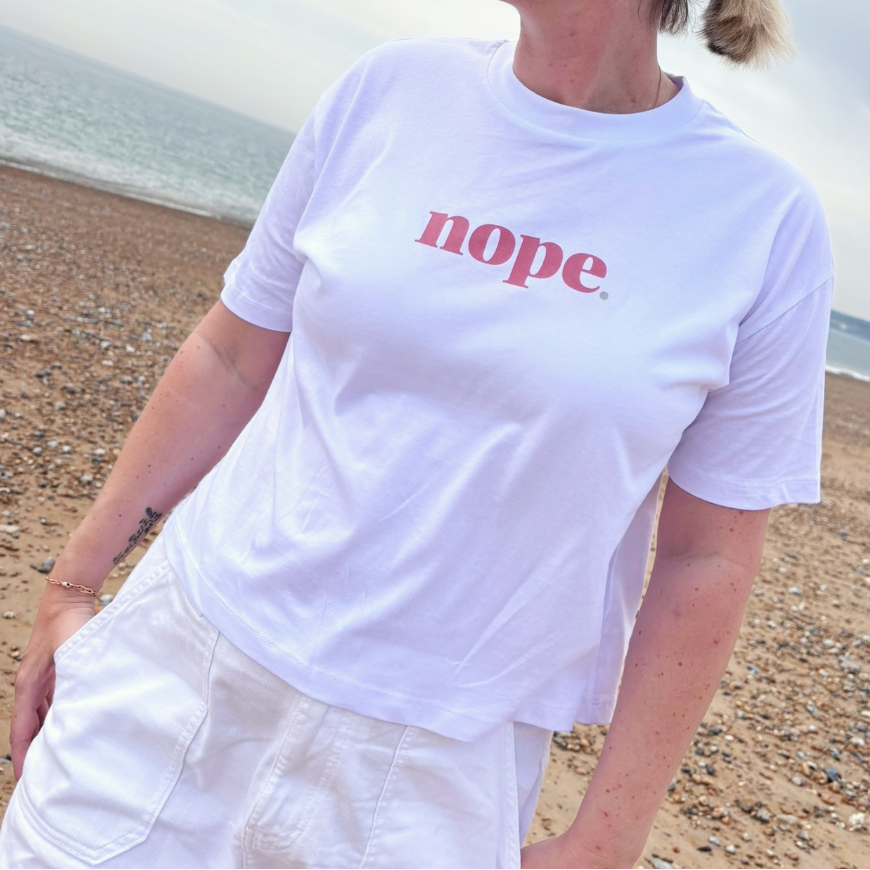 Person wearing a this is mabel boxy white t-shirt with 'nope' printed on it at the beach.