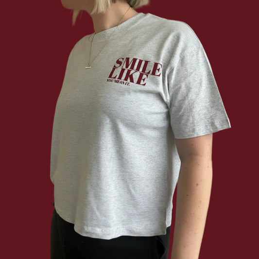 Person wearing a heather grey boxy t-shirt with red smile like you mean it mabel t-shirt 
