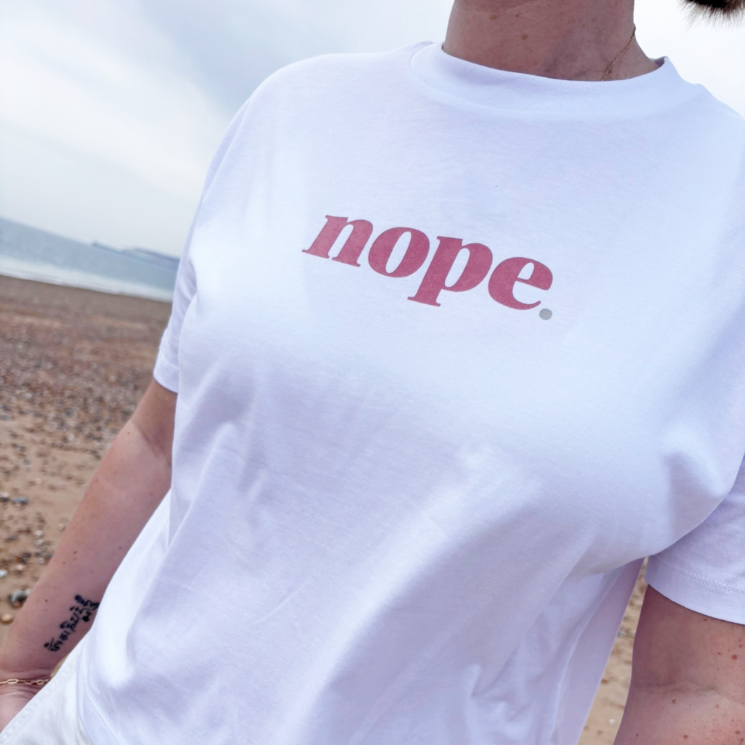 Person wearing a this is mabel white t-shirt with 'nope' printed on it at the beach.